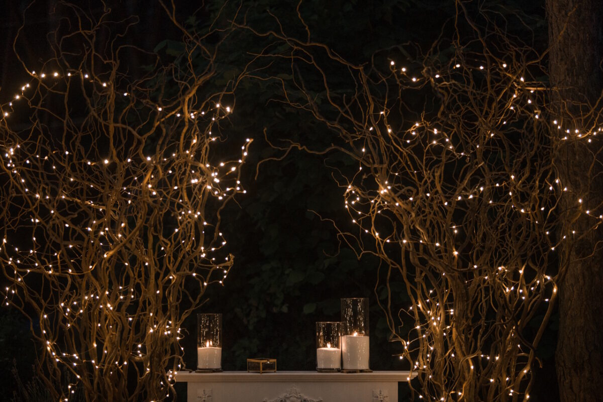 Высокие вазы с белыми свечами стоят под блестящими ветвями.